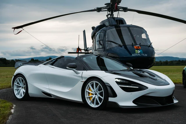 A white McLaren parked in front of a helicopter