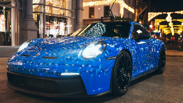 A blue Porsche beneath city Christmas lights