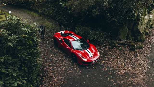 An aerial photograph of a red Ferrari on a woodland road