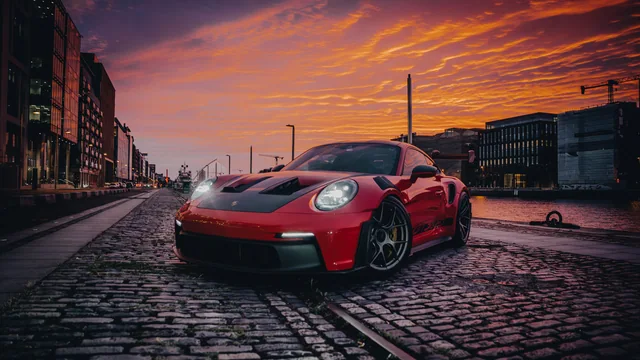 A red Porsche beside the river under a vivid evening sky