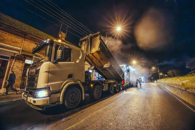 A work truck and road crew illuminated during night works