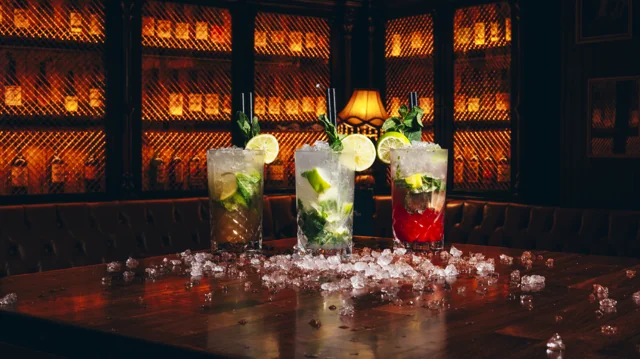 Three cocktails arranged on a bar table with warm amber lighting