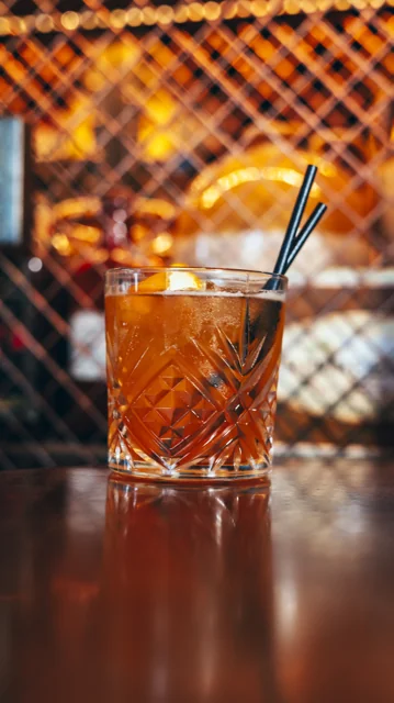 An amber cocktail with citrus garnish and a glass straw