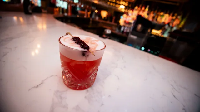 A pink cocktail topped with foam and a delicate garnish