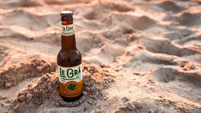 A Le Grá bottle on the sand in warm coastal light