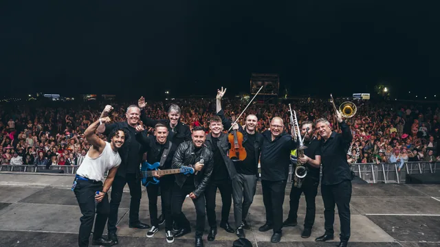 The band together on stage with the crowd behind them