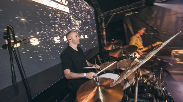 A drummer performing under stage lighting