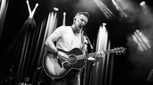 A black and white live photograph of Johnny Brady with his guitar