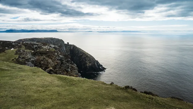 Coastal cliffs and calm water under a cloudy sky